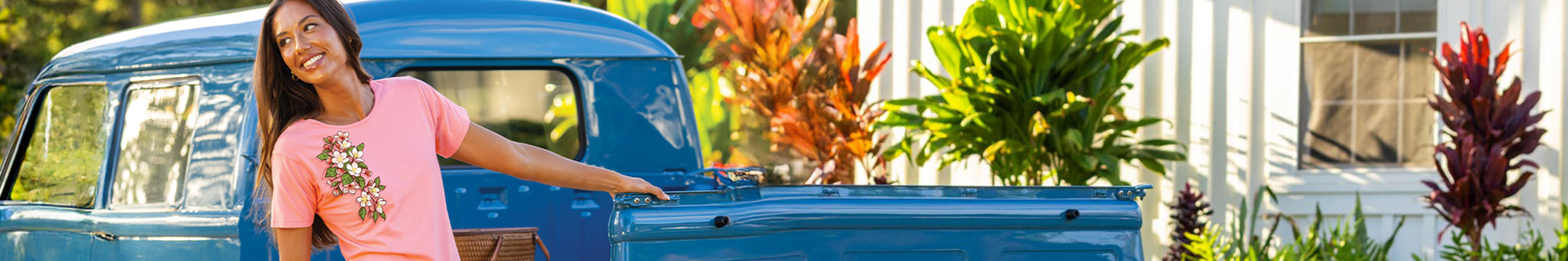 Woman standing next to a vintage blue truck with plants in the background