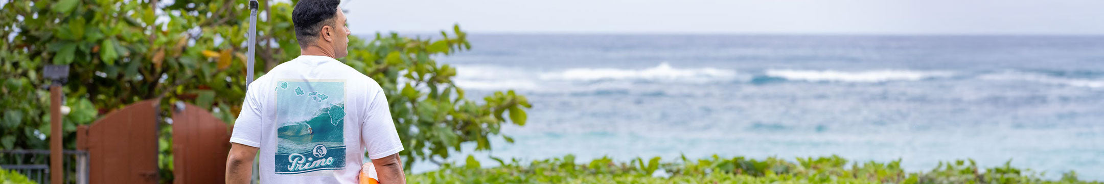 Person wearing a white t-shirt with a logo, standing by the ocean.