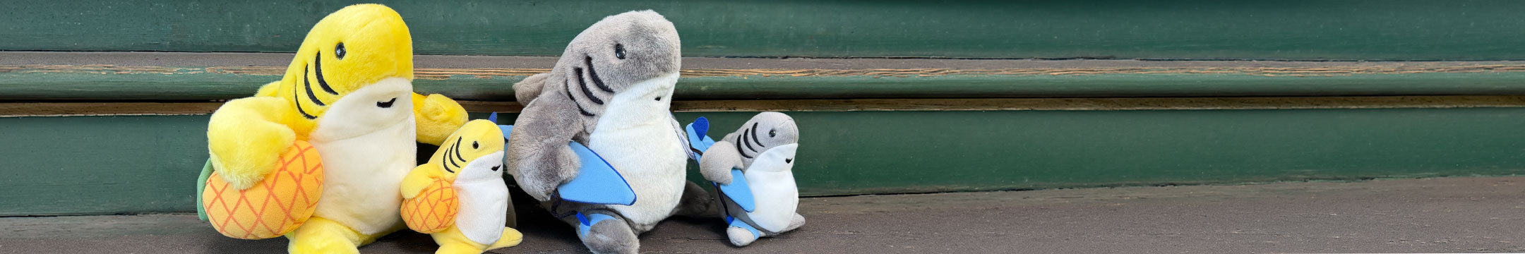 Four plush toys resembling a shark, a whale, and two smaller creatures on a green and gray background.