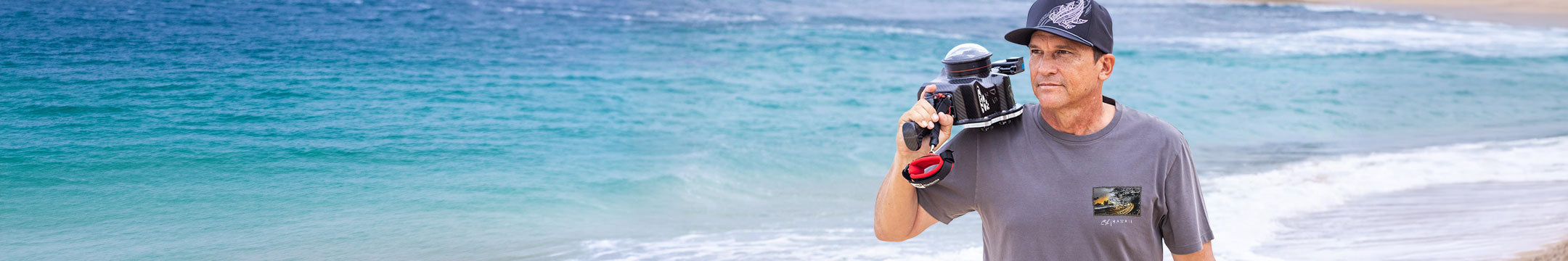 Man holding a camera on a beach with clear blue water