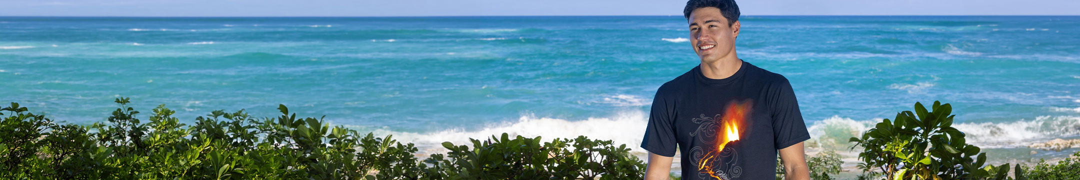 Man wearing a black t-shirt with a graphic design, standing in a natural setting along the beach with greenery.