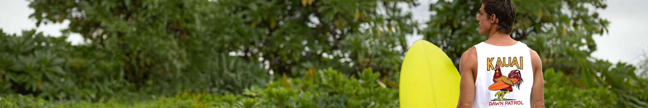 Person holding a yellow surfboard with 'Kauai' and tropical design on a green background