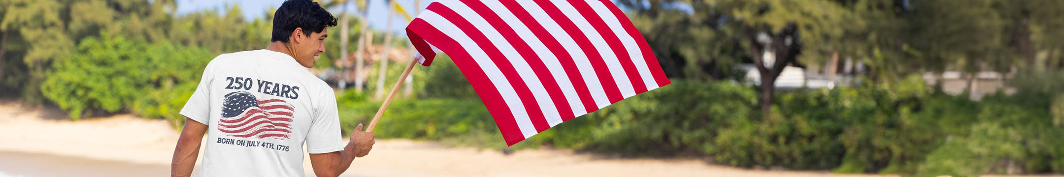 Person holding an American flag on a beach with greenery in the background