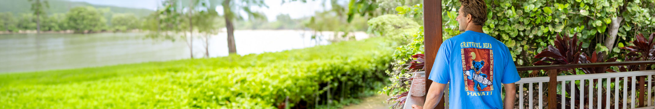 Person standing by a lake with greenery and a wooden fence in the background