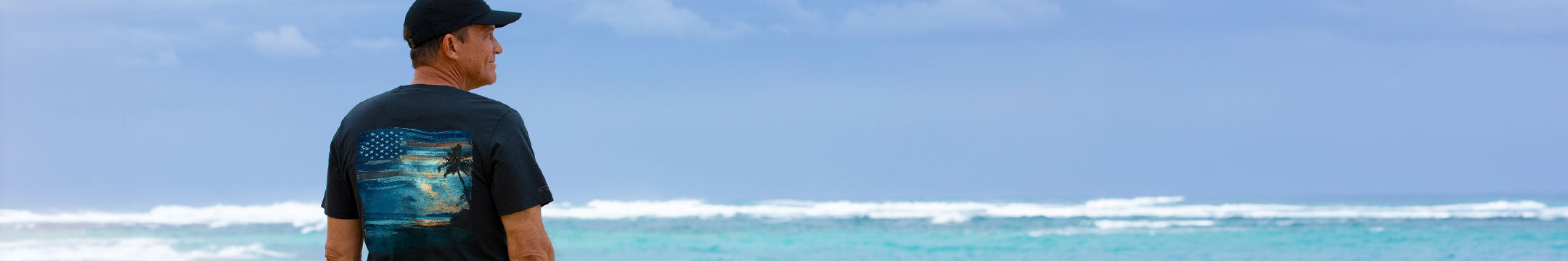 Man standing in front of a beach wearing a black shirt with a patriotic island design