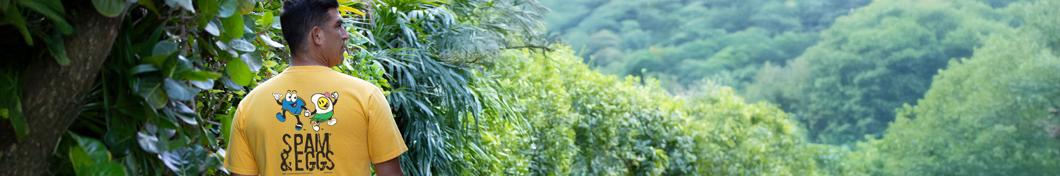 Person wearing a yellow t-shirt with text, standing in a lush green forest.