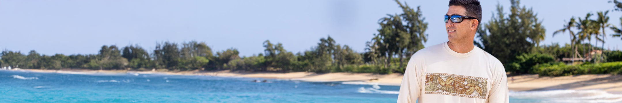 Man standing on a beach with clear blue water and greenery in the background
