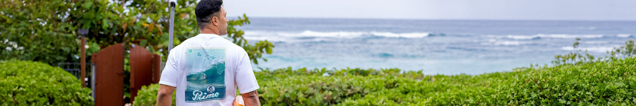 Man carrying a paddle board looking out at the ocean wearing a t-shirt with a surfing graphic design