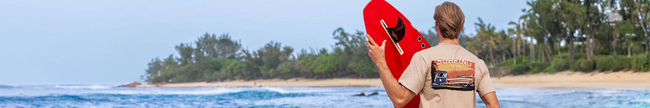 Man holding a red surfboard on a beach with palm trees in the background