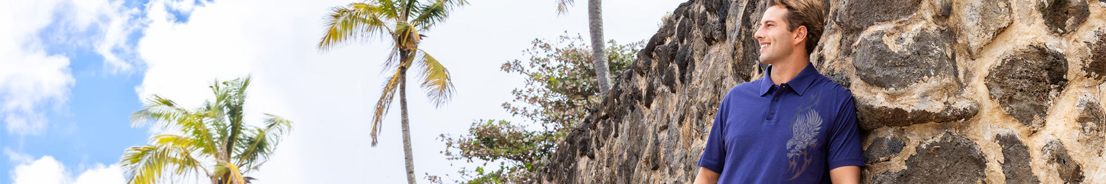 Man leaning against a stone wall with palm trees and blue sky in the background