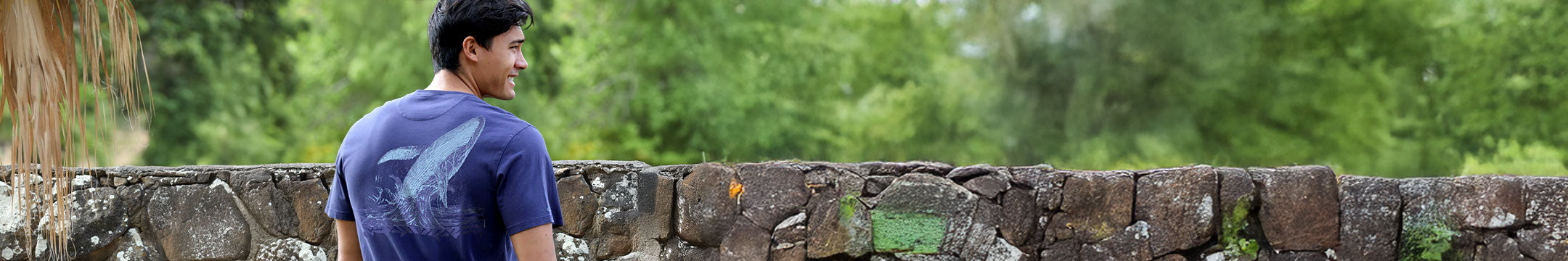 Person wearing a blue shirt standing on a stone wall with greenery in the background