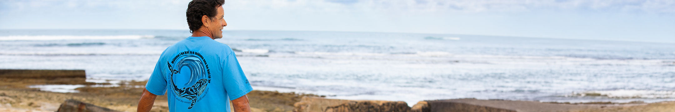 Person wearing a blue t-shirt with a graphic design, standing on a beach.