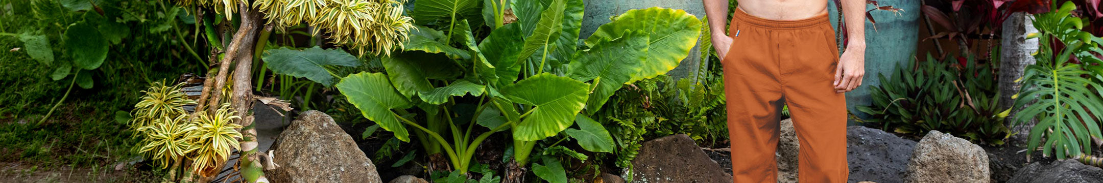 Person wearing orange pants standing in a garden with green plants and rocks.