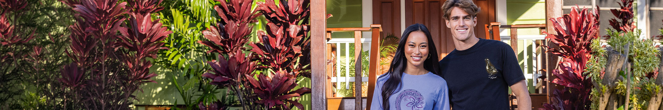 Two people standing in front of a house with lush greenery and flowers.