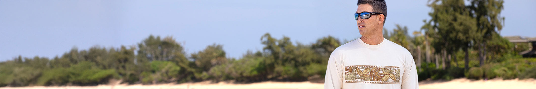 Man wearing sunglasses and a white shirt with text standing outdoors with trees in the background