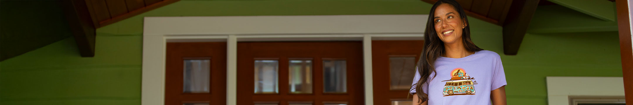 Woman standing in front of a green building with wooden doors wearing a lavender shirt