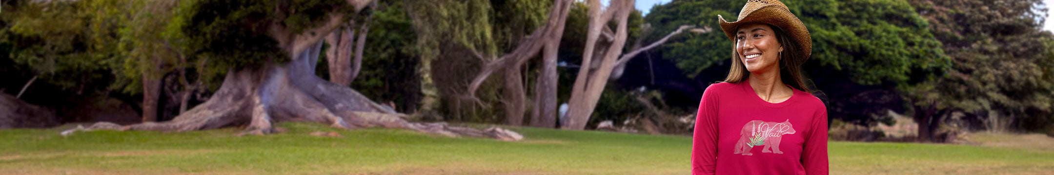 Woman in a red shirt and hat standing in a grassy area with trees in the background