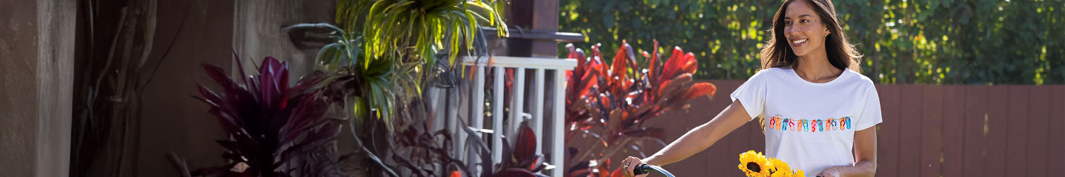 Woman holding sunflowers in a garden setting with plants and a white fence.