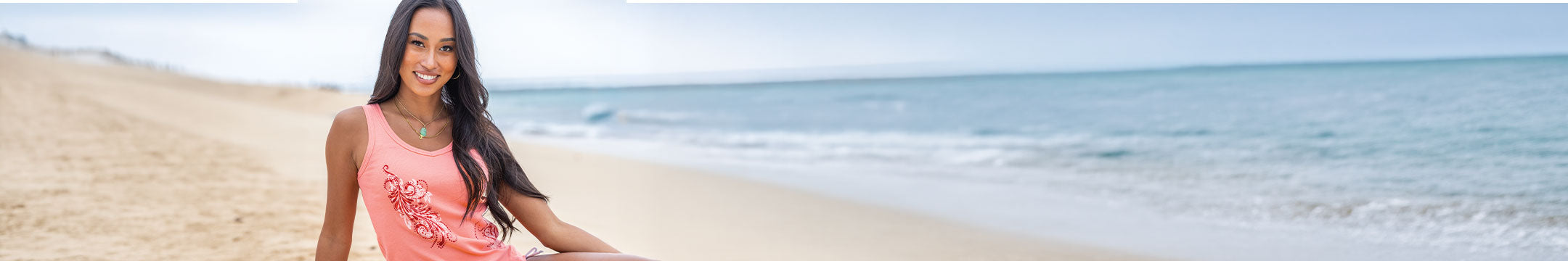 Woman in a pink tank top standing on a beach with ocean in the background