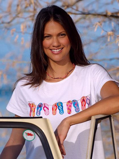 Woman wearing a white t-shirt with colorful flip-flop design, standing outdoors.
