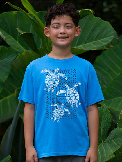 Child wearing a blue t-shirt with turtle design in front of green foliage