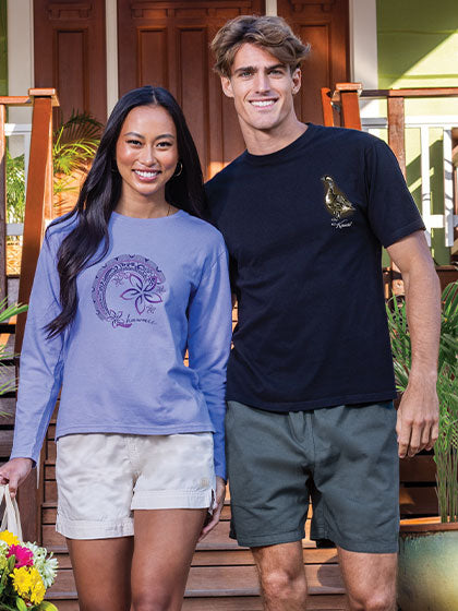 Two people standing outdoors, one wearing a blue long-sleeve shirt with a logo and the other in a black t-shirt with a logo.