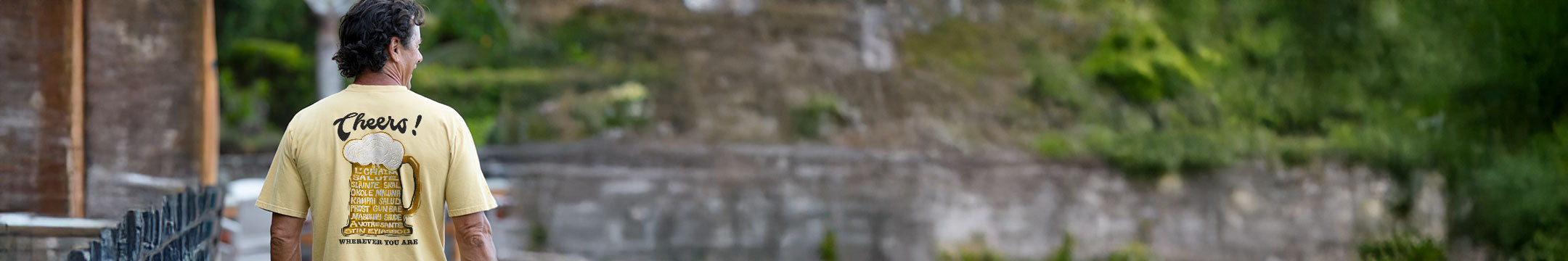 Person wearing a beer dyed  t-shirt with text and graphics, standing in front of stone steps and greenery.