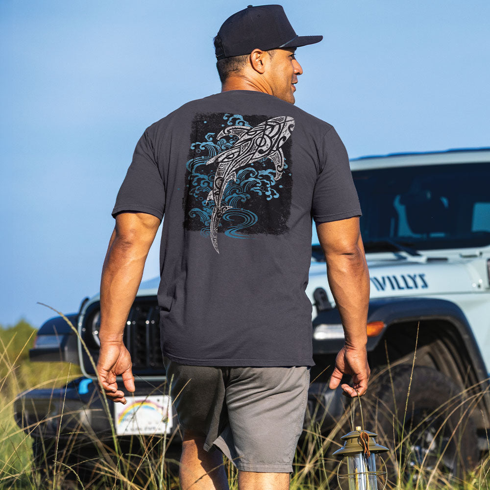 A man wearing a navy blue t-shirt with a large shark graphic on the back, walking outdoors near a white Jeep with 'WILLYS' on the side.