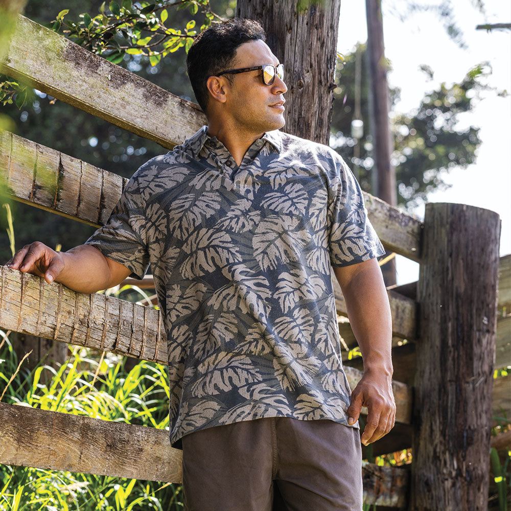 Man wearing a hawaiian polo standing in front of a fence