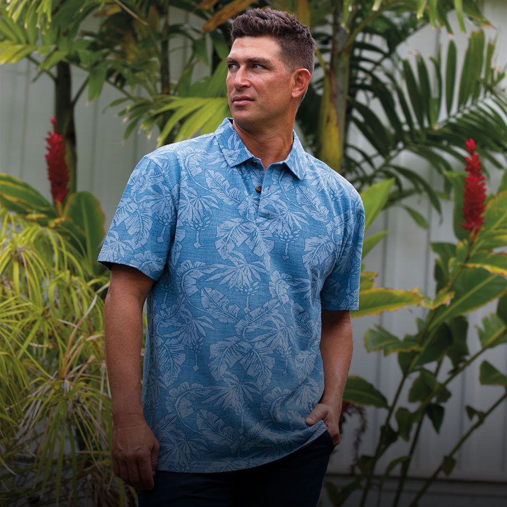 Man wearing a blue patterned shirt standing among tropical plants.