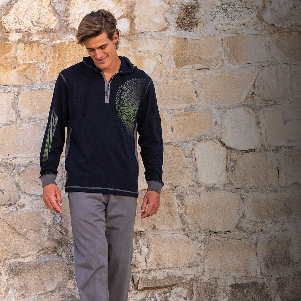Man wearing a dark blue pullover with a green emblem against a stone wall.