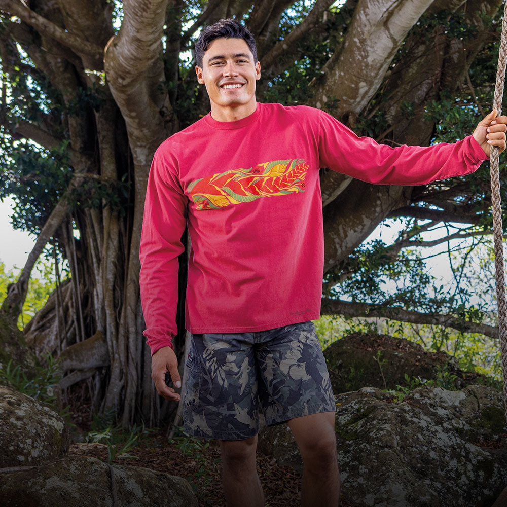 Man wearing a red long-sleeve shirt with a colorful design, standing outdoors near a large tree.