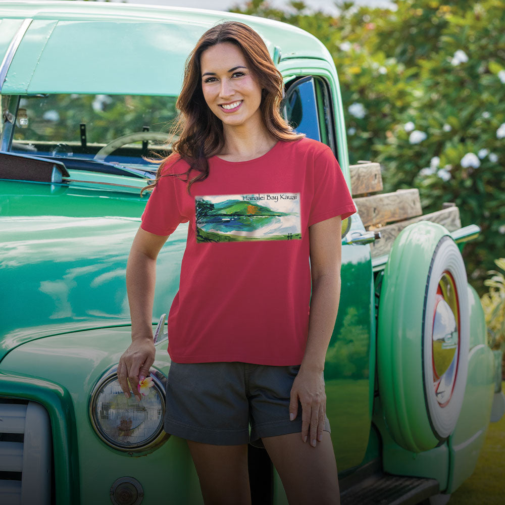 Woman wearing a red t-shirt with a graphic design, standing next to a vintage green truck.