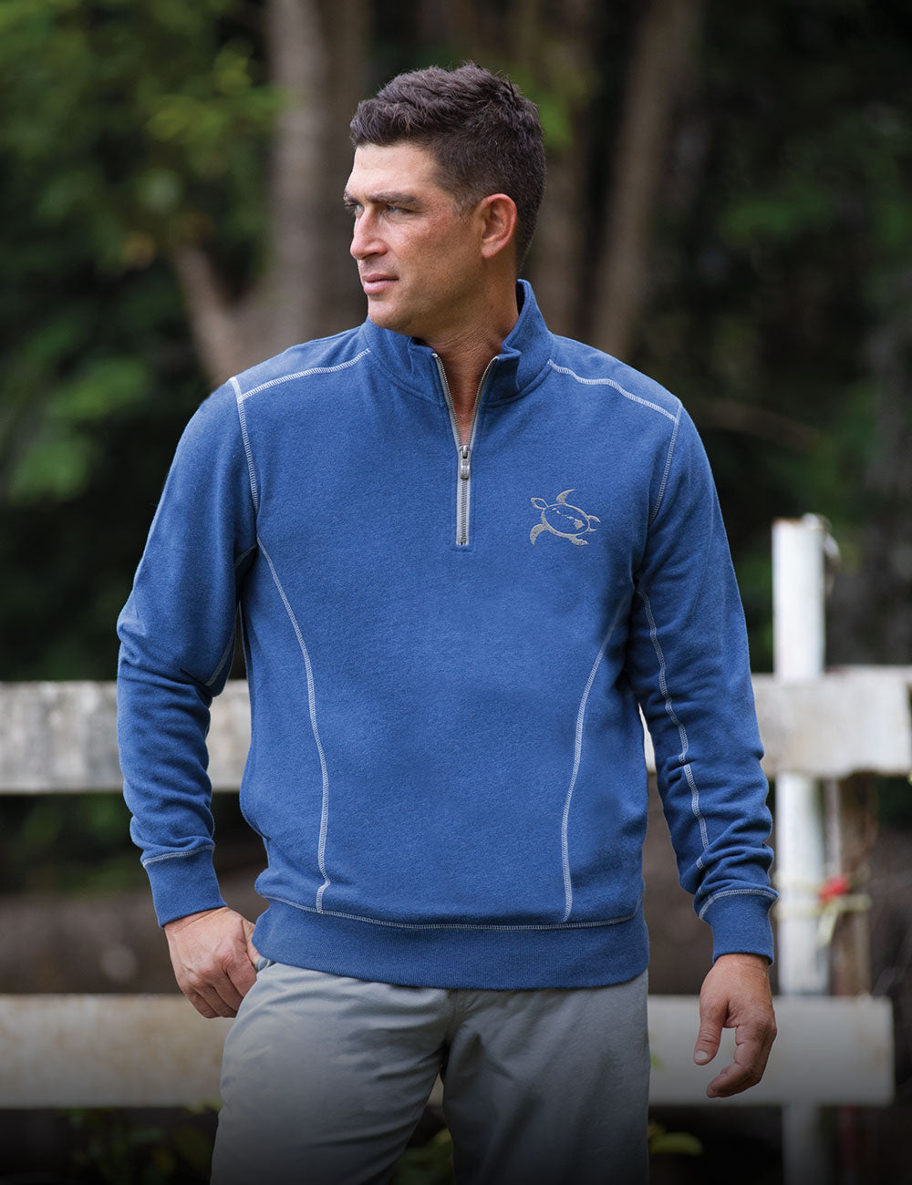 Man wearing a blue fleece pullover with a logo, standing outdoors.