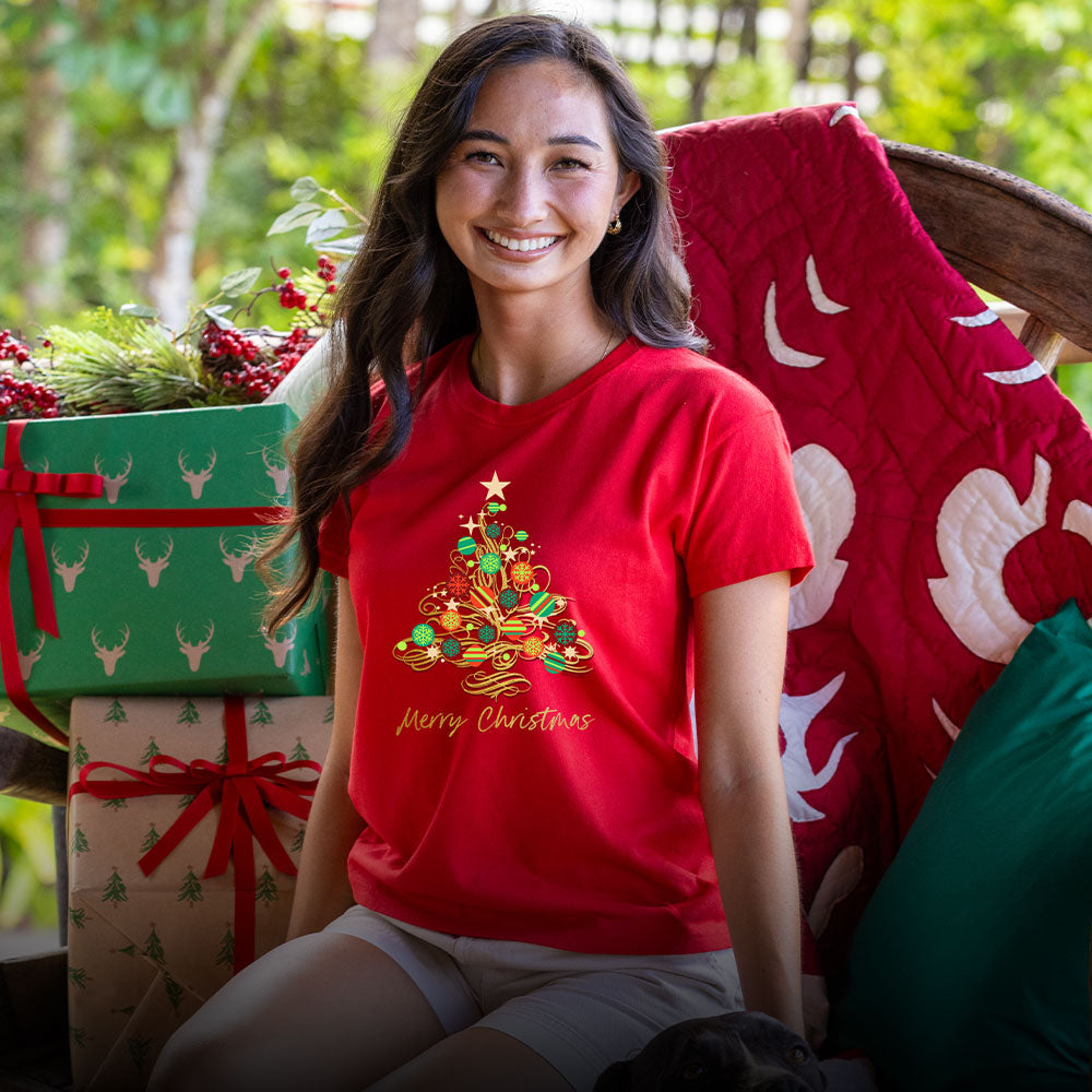 Woman wearing a red Christmas-themed t-shirt with presents and greenery in the background