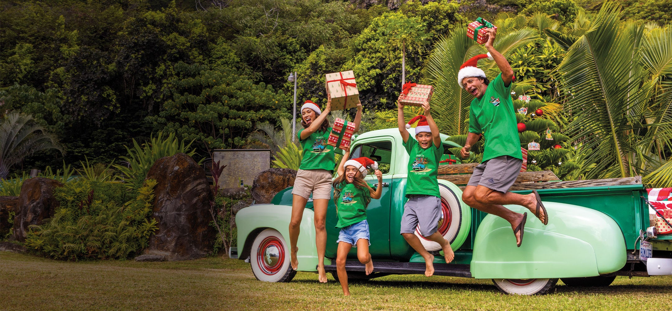 Family with children in Christmas outfits standing around a vintage truck with Christmas decorations outdoors.