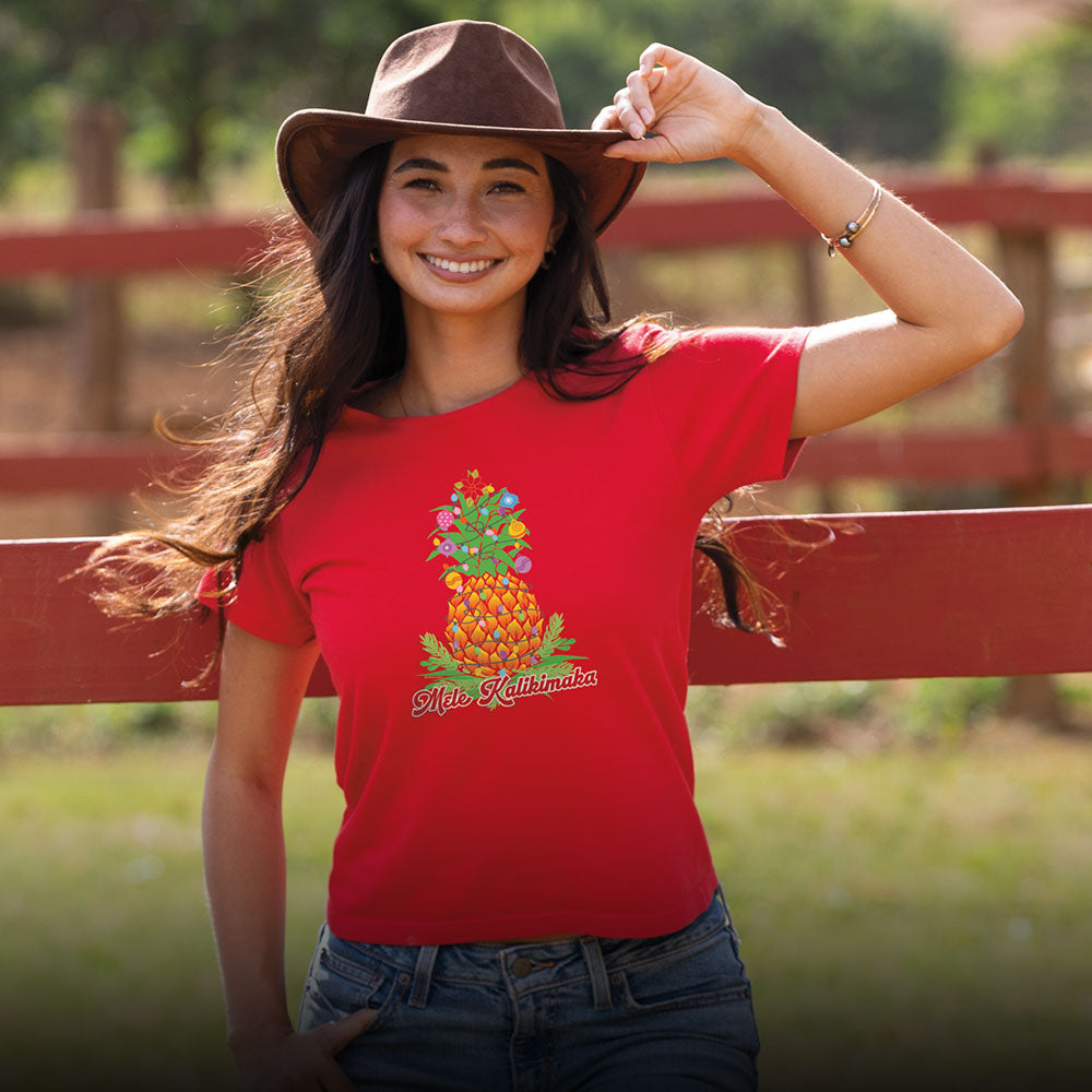 Woman wearing a red t-shirt with a pineapple design and text, standing outdoors near a wooden fence.
