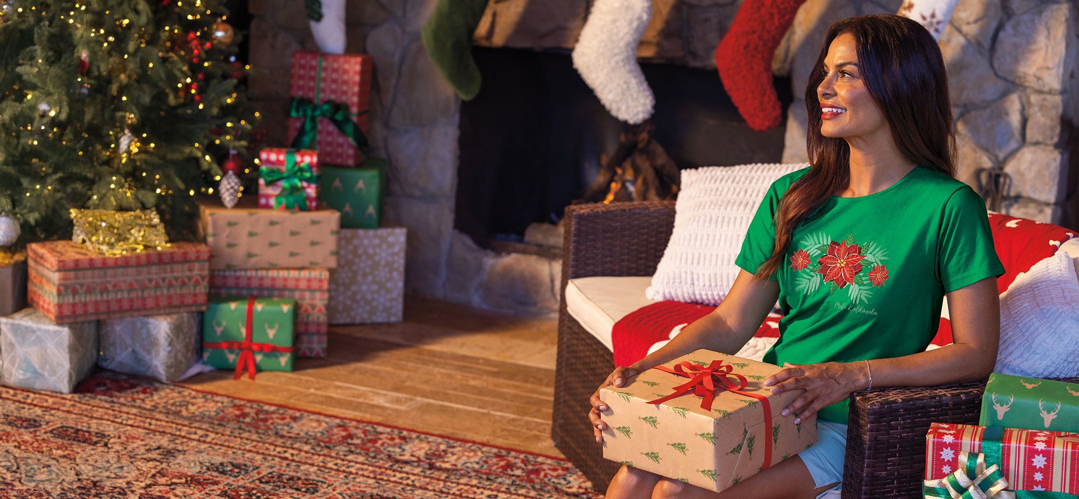 Woman in a green Christmas-themed shirt holding a gift in a festive living room.