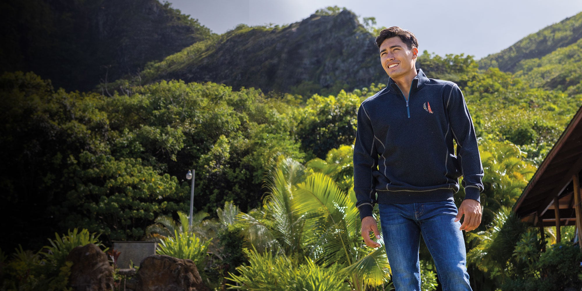 Man standing outdoors with greenery and mountains in the background