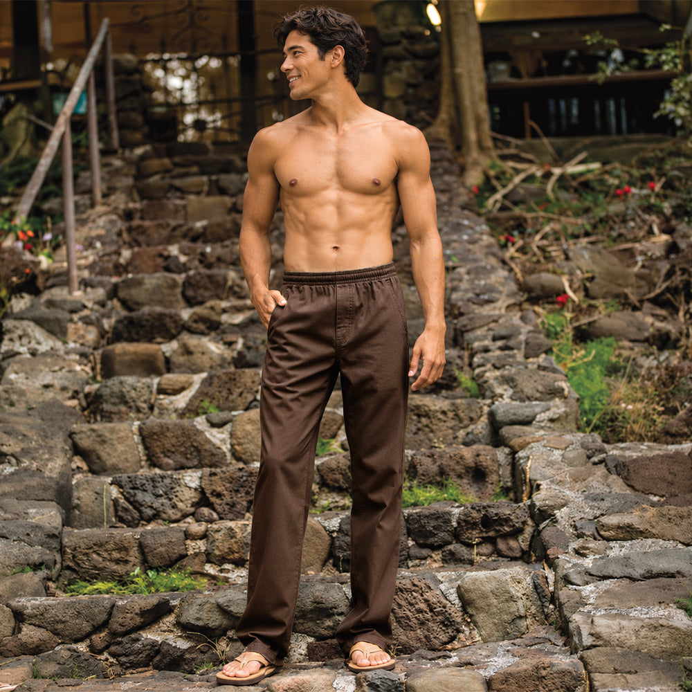 A shirtless man wearing light olive green drawstring pants and sandals, standing on stone steps outdoors.