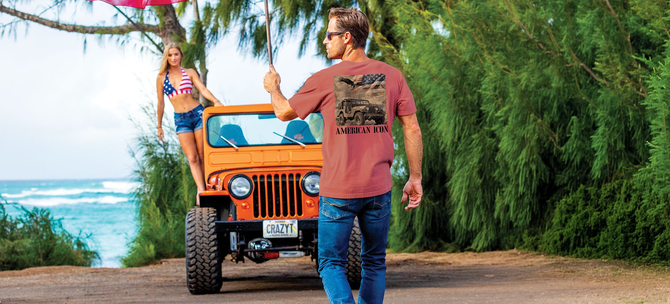 Man walking towards an orange Jeep with a woman standing nearby, set against a scenic beach backdrop.