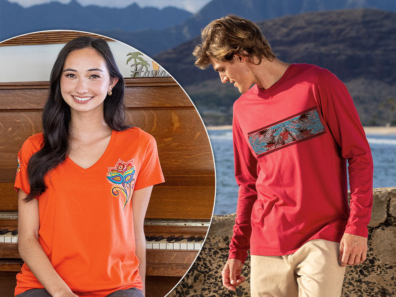 Woman in orange shirt with butterfly design and man in red shirt with graphic design by water and mountains.