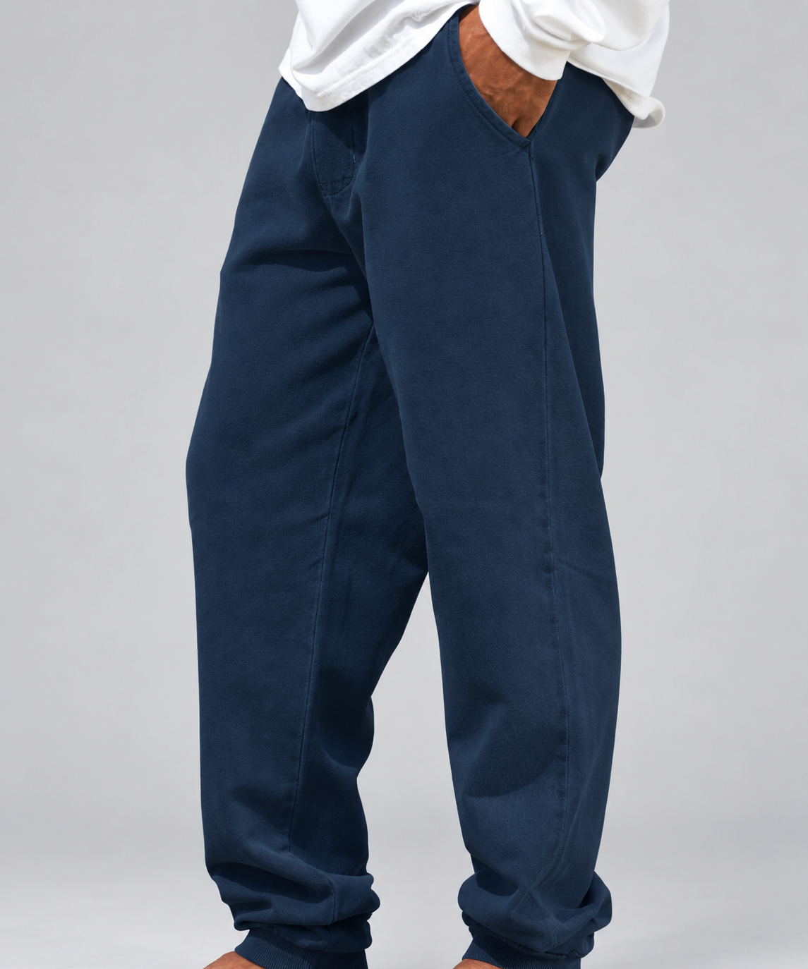 A person wearing loose, dark navy jogger-style pants with side pockets and a white shirt tucked in, photographed against a light gray studio background.