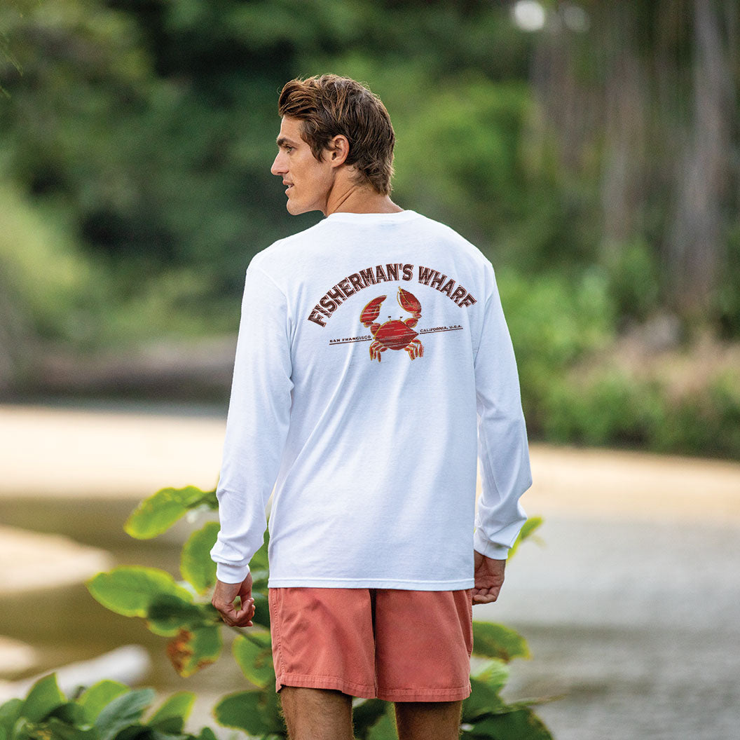 Man wearing a white long-sleeve shirt with 'Fisherman's Wharf' logo outdoors.