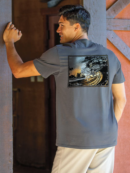 Man wearing a gray t-shirt with a graphic design on the back, standing against a rustic wooden door.