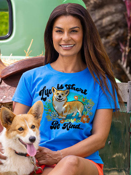 Woman wearing a Blue Hawai Dyed t-shirt with a dog graphic and text, sitting next to a corgi.