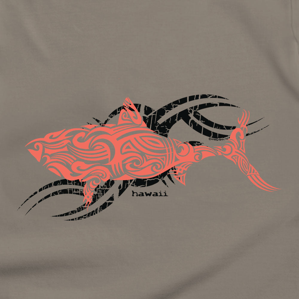 A close-up of a taupe-gray t-shirt featuring a Polynesian-inspired shark graphic in coral orange and black, with the word 'hawaii' printed in black below the shark.