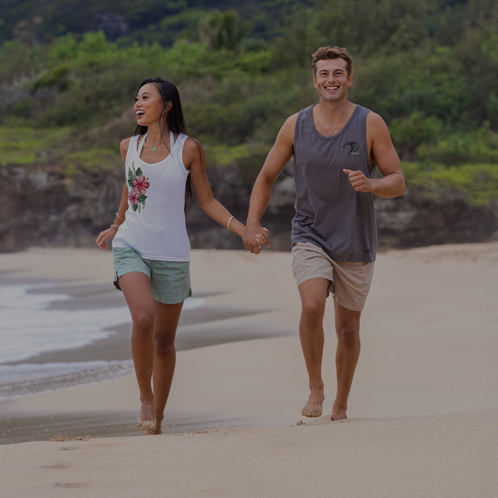 Man and woman walking hand in hand on a sandy beach with greenery in the background