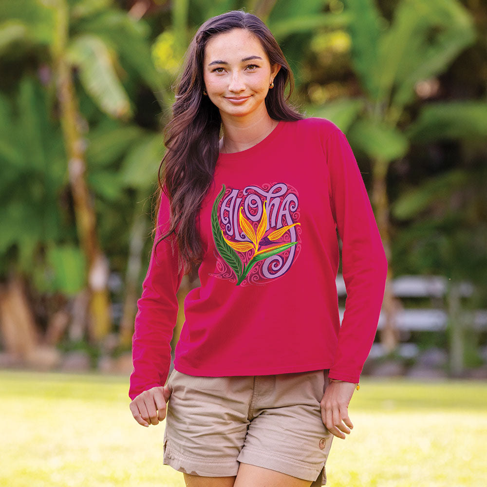 Woman wearing a pink long-sleeve shirt with a colorful design outdoors.