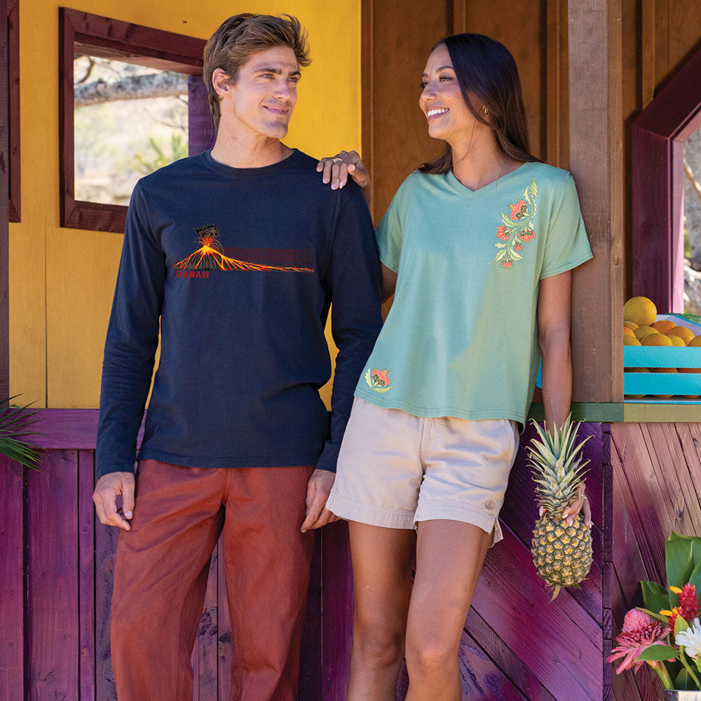 Two people standing in front of a colorful wooden cabin, one wearing a navy long-sleeve shirt and the other in a green t-shirt with a pineapple graphic.
